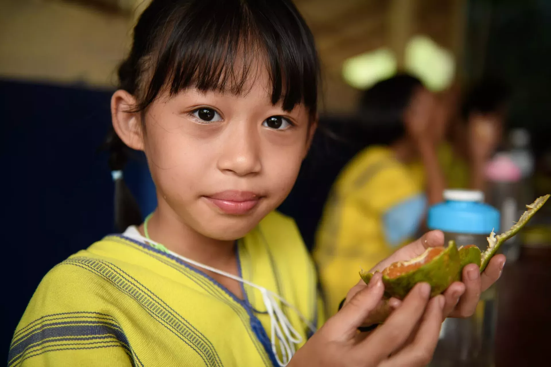 A girl student is looking at the camera with orange in her hands