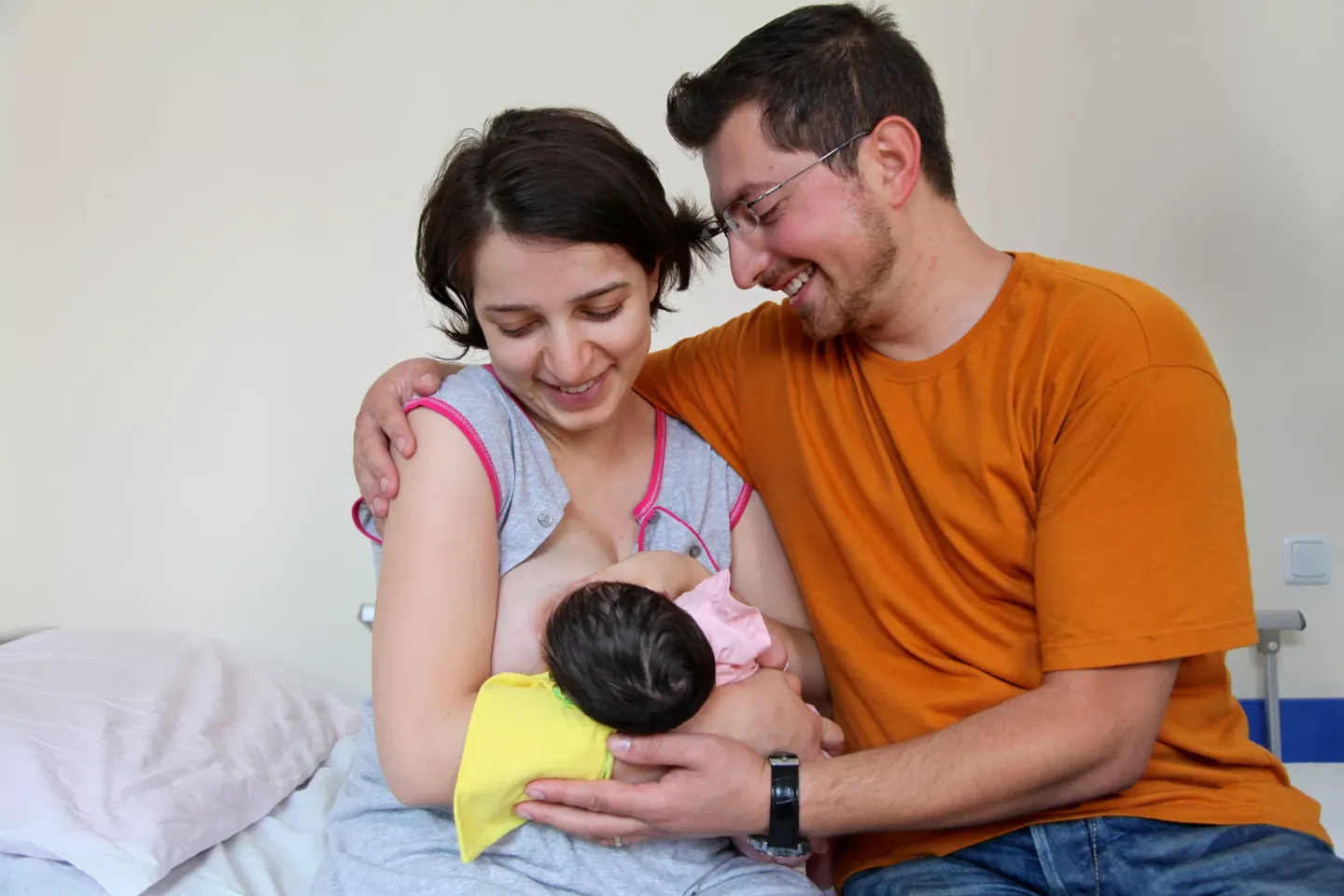 Mother is breastfeeding her new born baby while the father accompanies them.