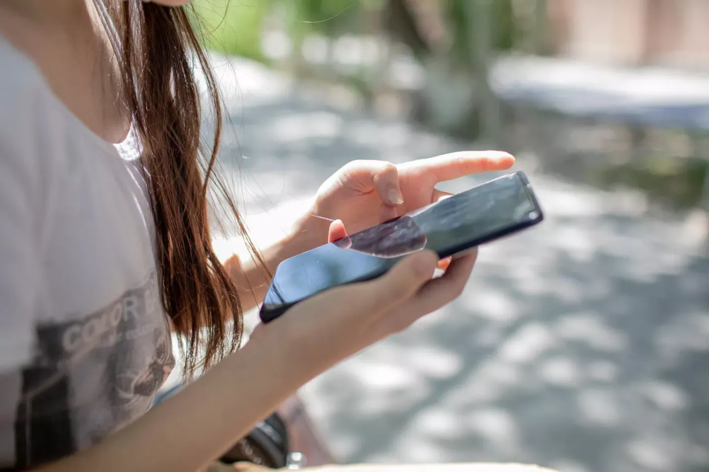 A girl sits on a park bench and looks at something on her phone,