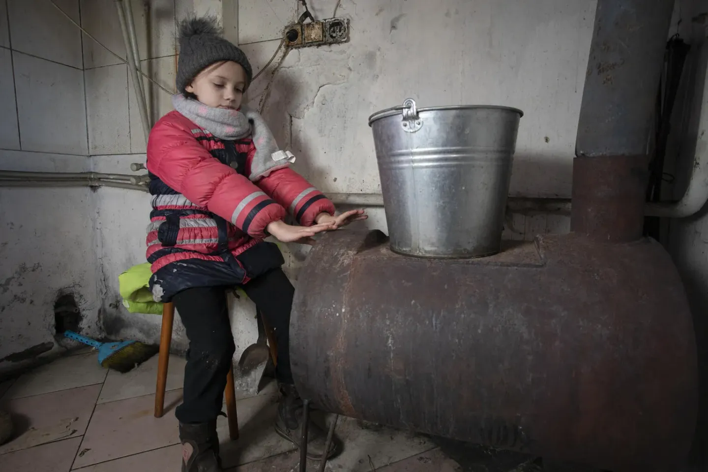 Nine-year-old Masha warms herself by the wood-burning stove in her home in eastern Ukraine in February 2022. While the stove brings needed heat in the cold winter, it can bring something else, too: indoor air pollution that can threaten children&rsquo;s health. 