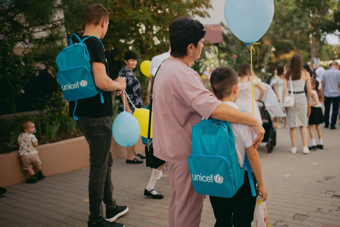 A woman is hugging a boy t the courtyard of the Prylymansk school. The boy is wearing a blue backpack - gift from UNICEF for the beginning of a school year.