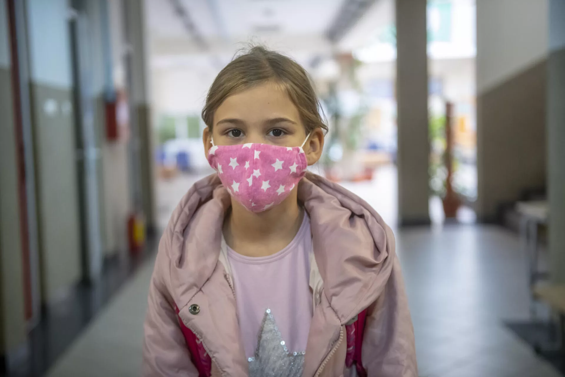 A girl wearing pink mask is standing in the school's corridor.