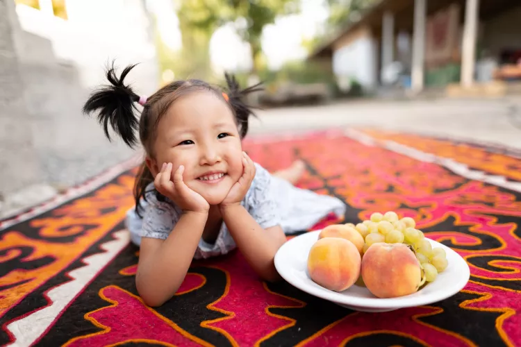 Child smiles next to plate of fruit.