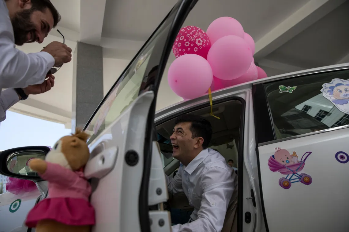A father smiles as he gets into his decorated car as part of the 'bringing the baby home' ritual.