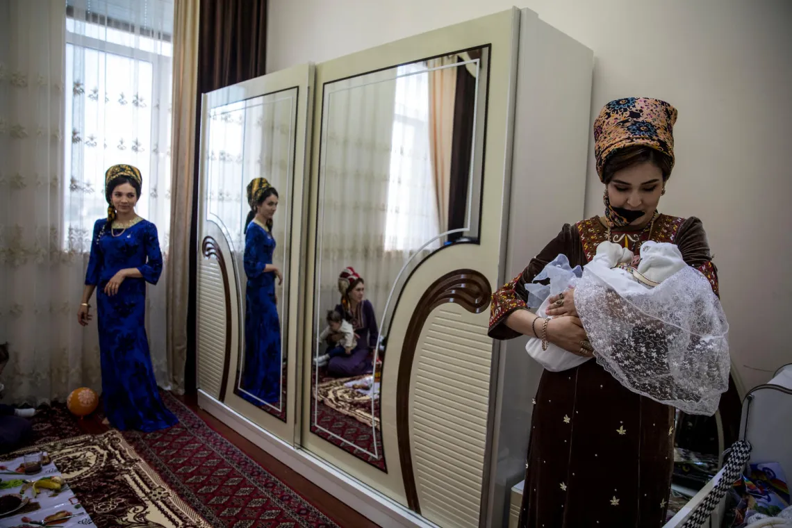 A mother gazes down at the newborn in her arms at home during family celebrations.