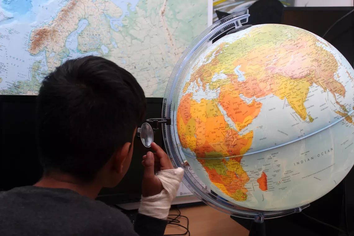 A boy uses a globe to describe his migration journey at Sedra temporary reception centre in Bosnia and Herzegovina. May 2021.