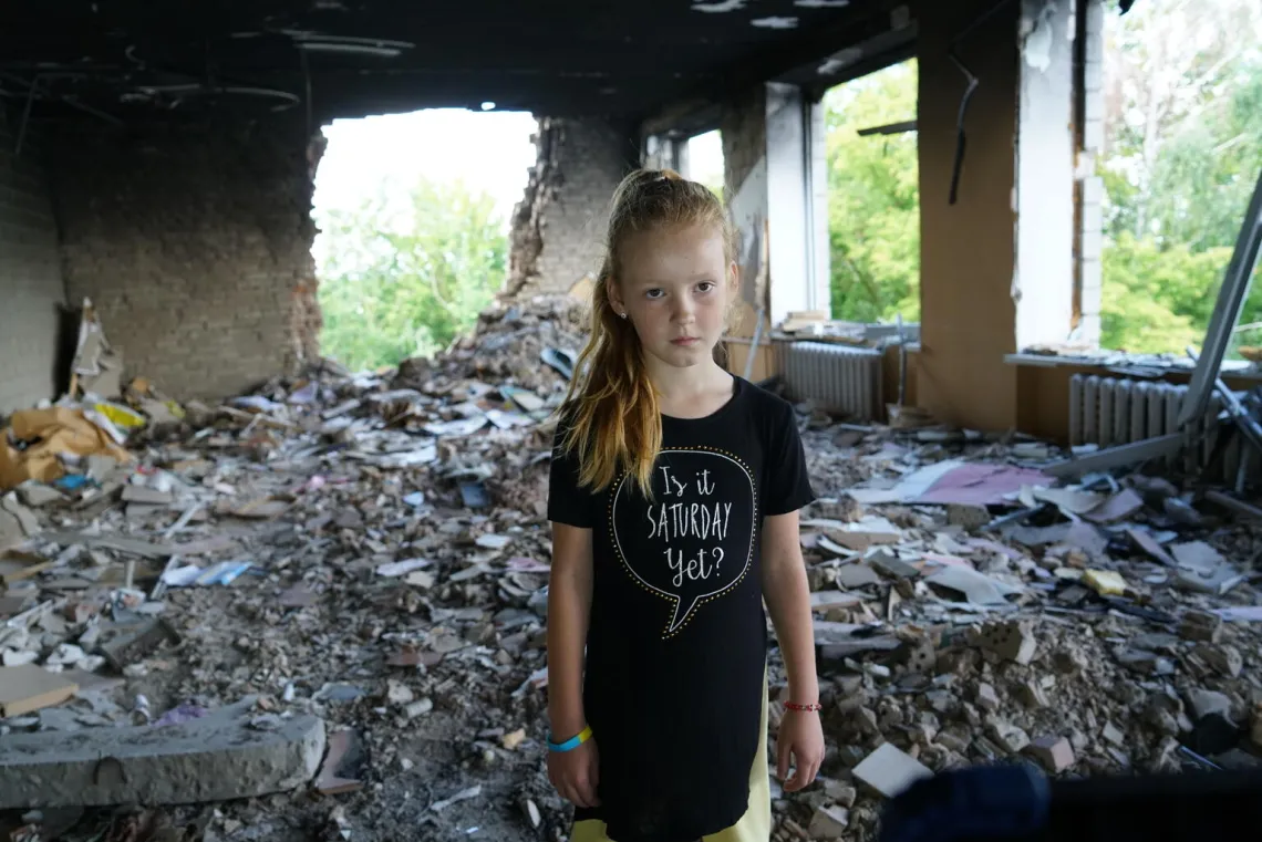  8-year-old Anya stands amidst rubble in her damaged school in Buzova, Ukraine.