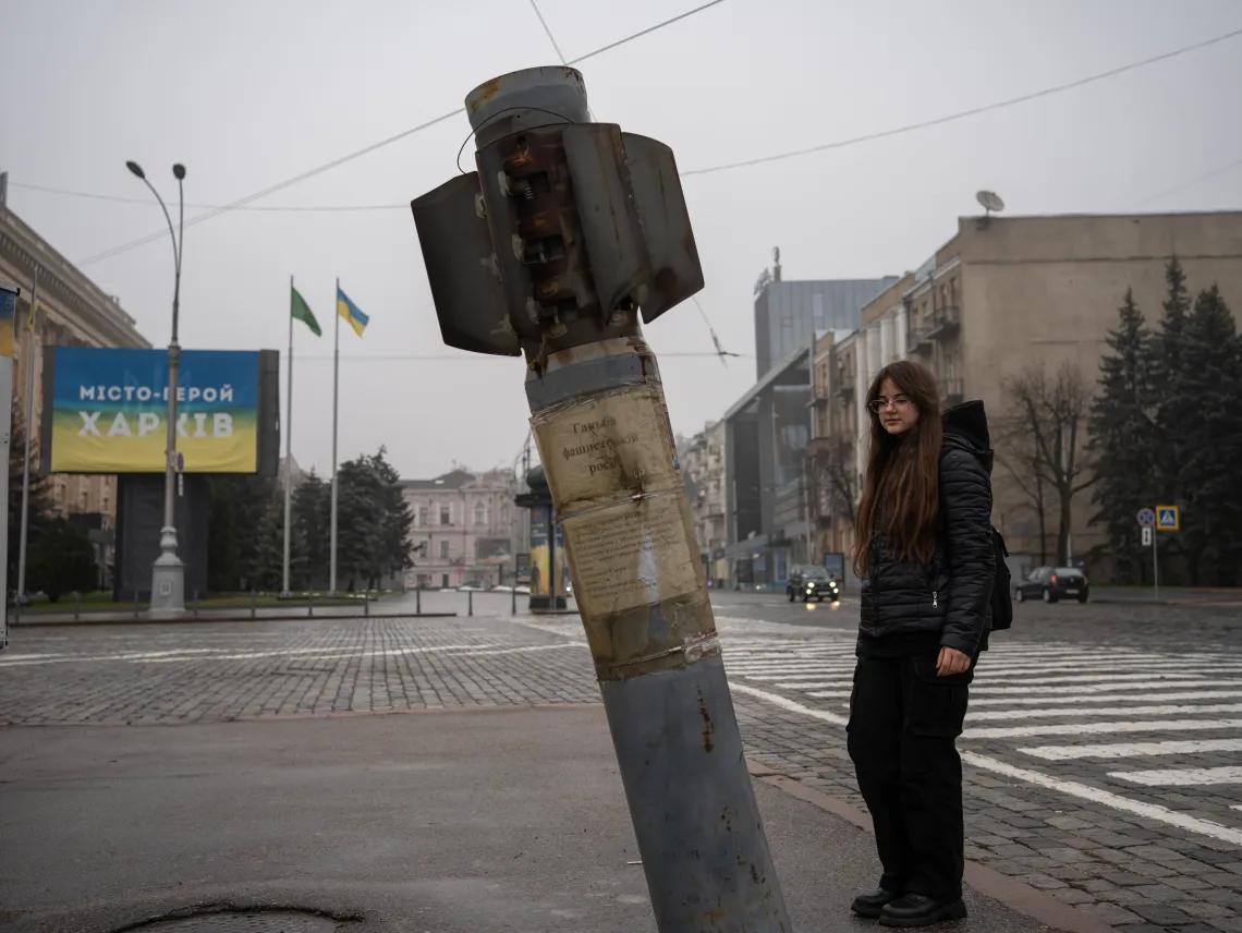 Nika (11) is standing on the road in the centre of Kharkiv, next to a huge rocket shell, that sticks out of the ground.