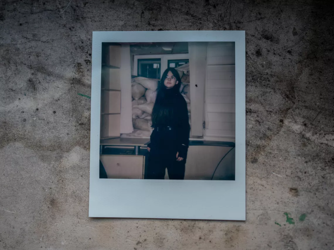 Polaroid picture from Nika's (11) photo album of memories, showing her next to the window, barricaded with sandbags, waiting for the air alarm to end at the shelter of Child Spilno Spot.