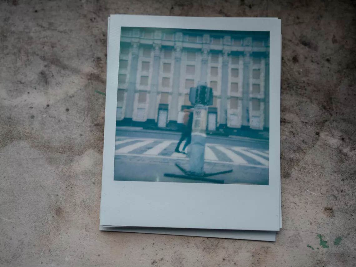 Polaroid picture from Nika's (11) photo album of memories, showing a huge shell in the ground in the centre of Kharkiv.