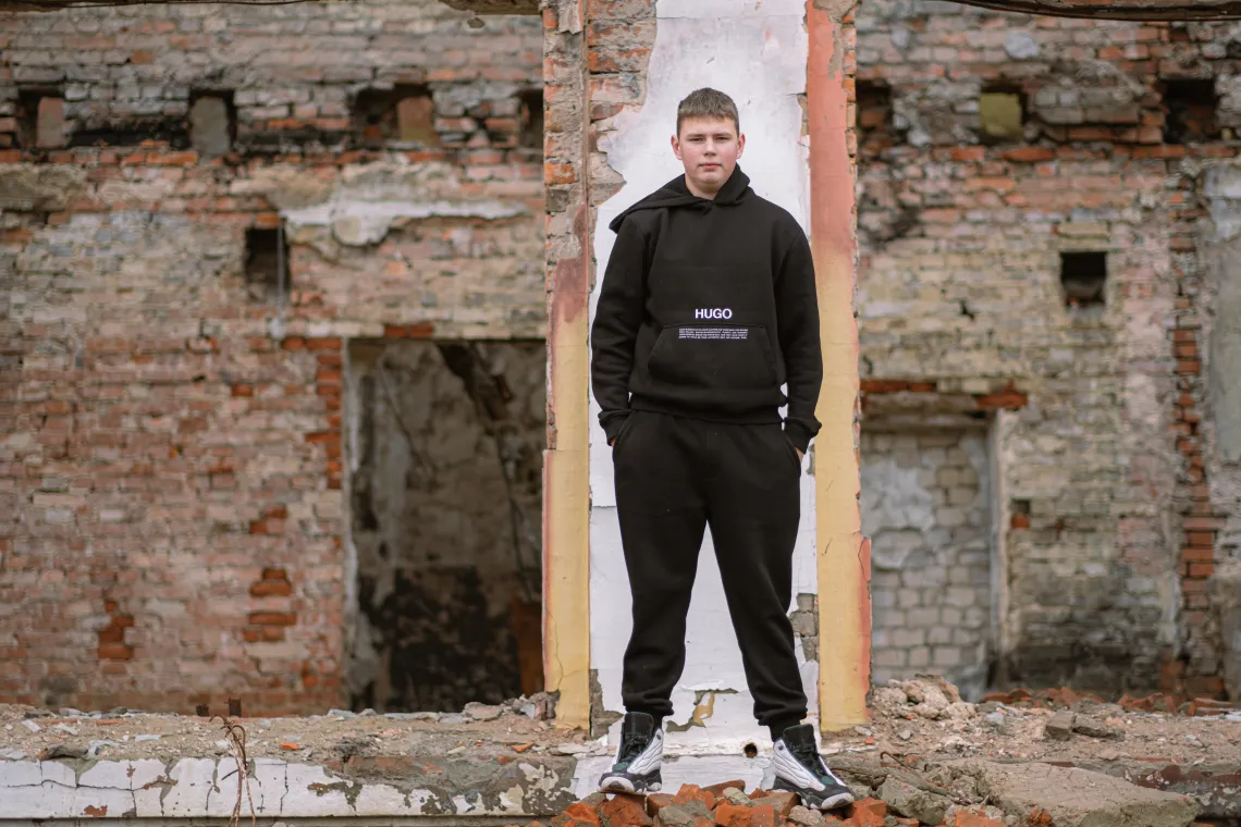  Stepan (15) is standing against the background of a destroyed school, he used to study in.