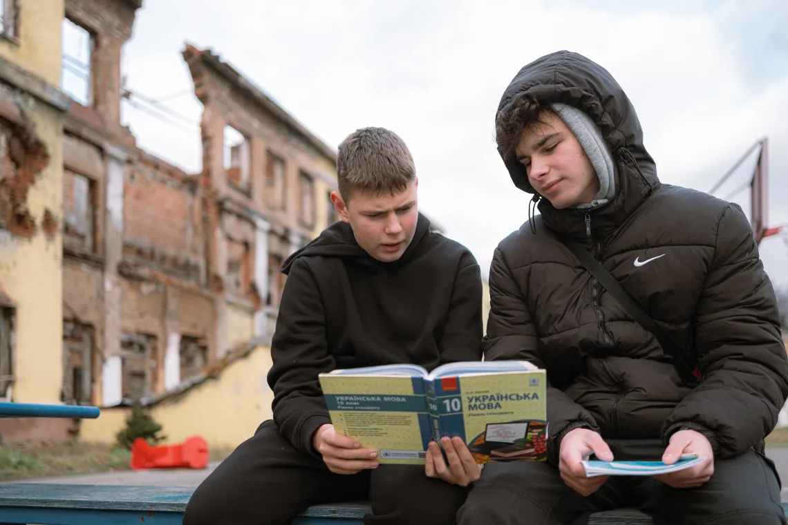 Stepan (15) and Yaroslav (16) read a textbook on Ukrainian against the background of a destroyed school, they used to study in.
