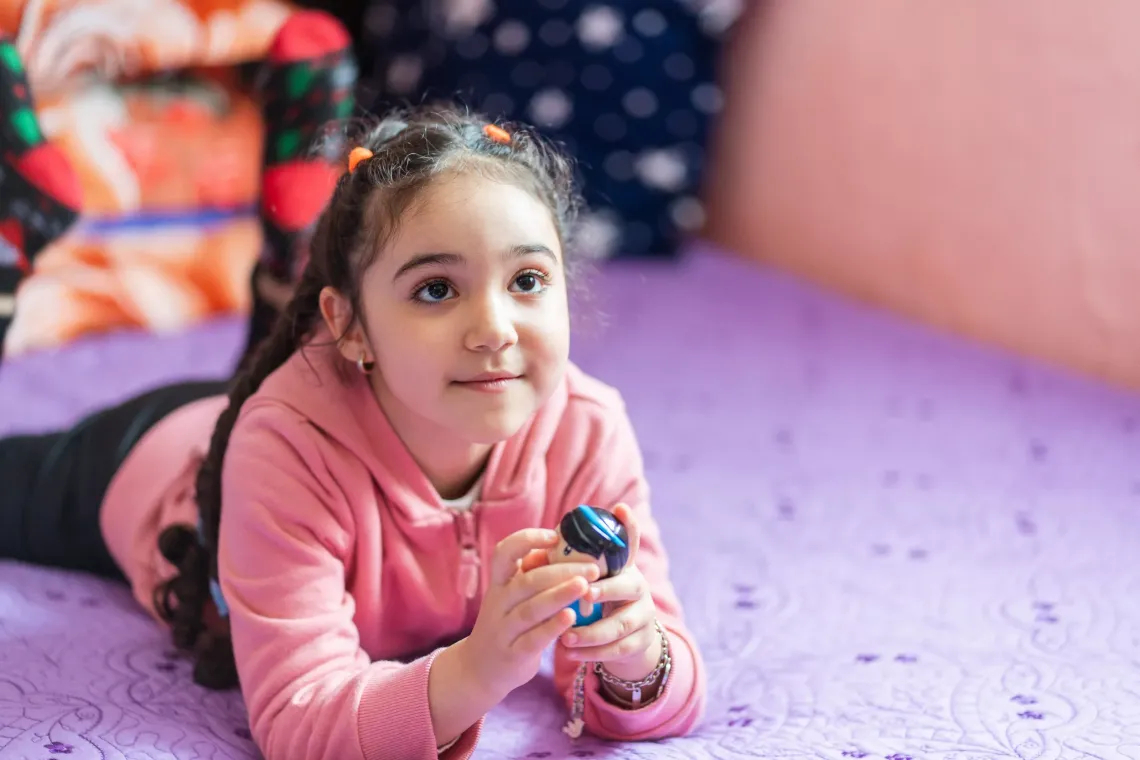 Antonia plays with a toy in bed in her house in February 2024. Her predisposition to health complications from respiratory infections, caused by having pneumonia when she was two, is why she must take extra care during recovery from even a simple cold.