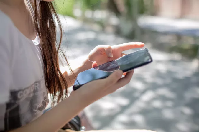 A girl sits on a park bench and looks at something on her phone,