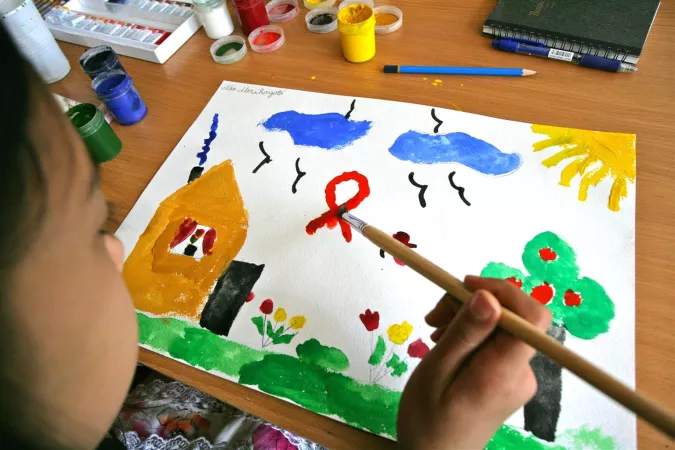 A child paints a scene showing a house with a HIV awareness ribbon in the sky.