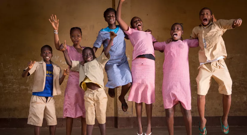 A group of children jump in the air with smiles on their faces in a classroom in Guinea. 