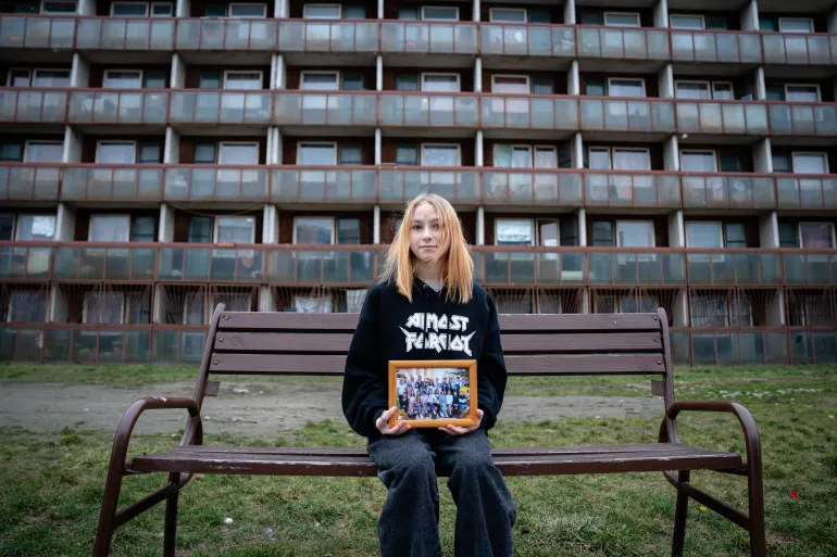 Vera sits in front of her accomodation centre holding a class photo from Ukraine.