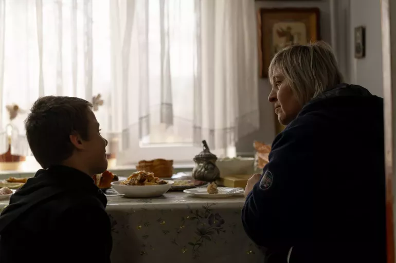 A boy and his foster mother talk at their kitchen table. 