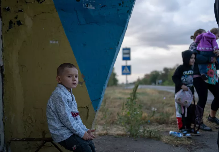 A boy sits on a bus station bench.