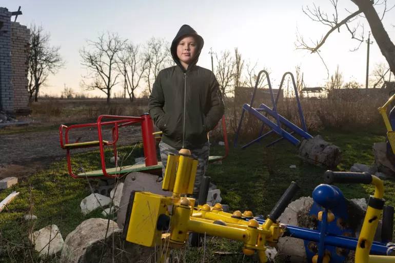 A boy stands in front of his destroyed school