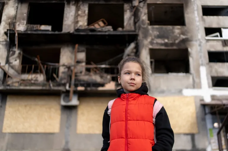 12 March 2025, Dobropillia, eastern Ukraine. Eight-year-old Myroslava stands in front of a bombed-out building.