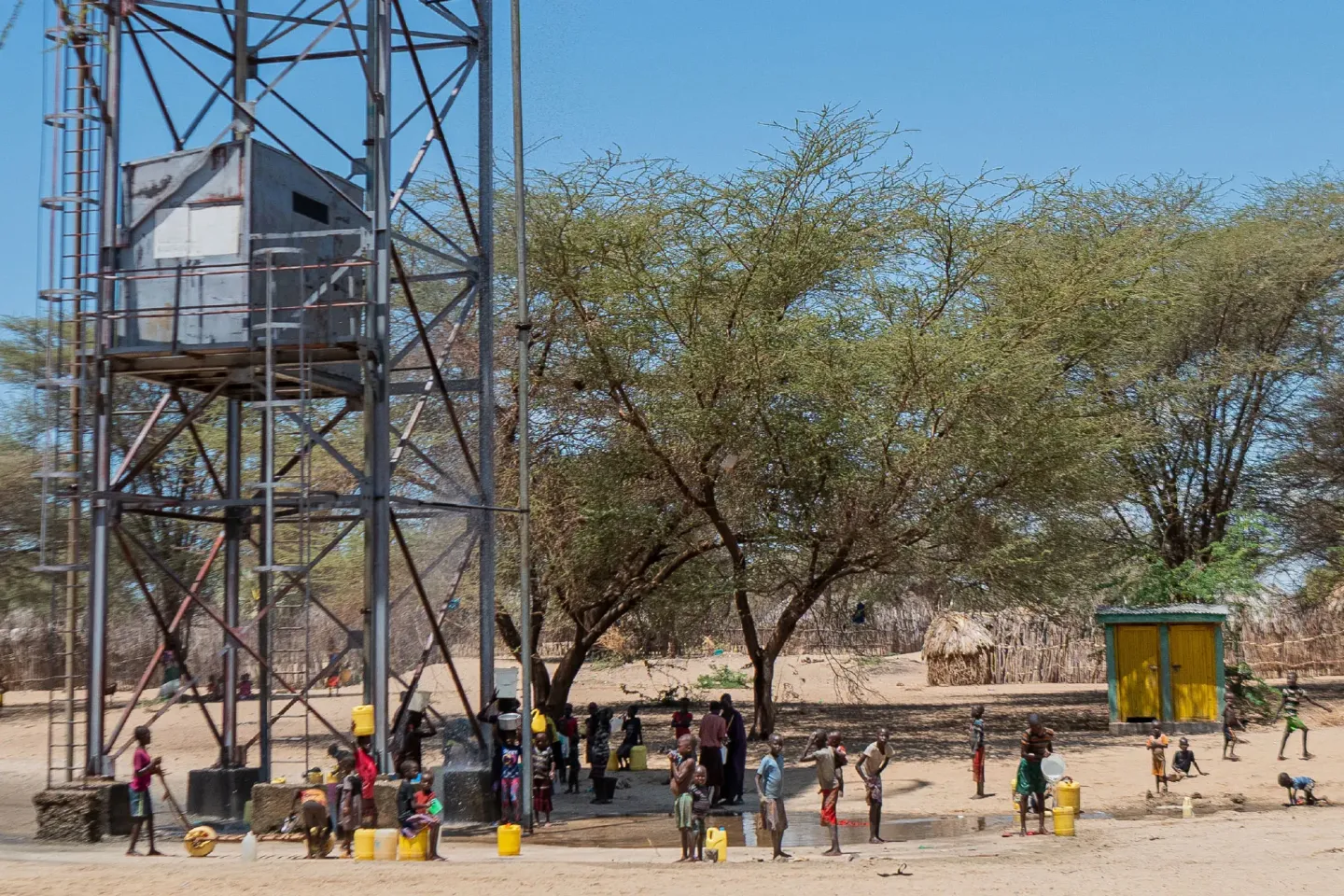 People standing with water cans below a water tower