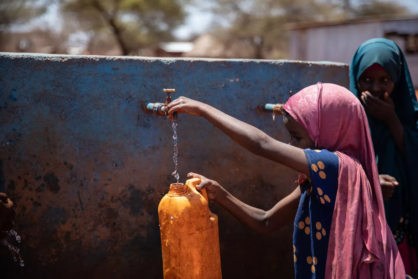 A girl fills a jug with water at an outdoor water source