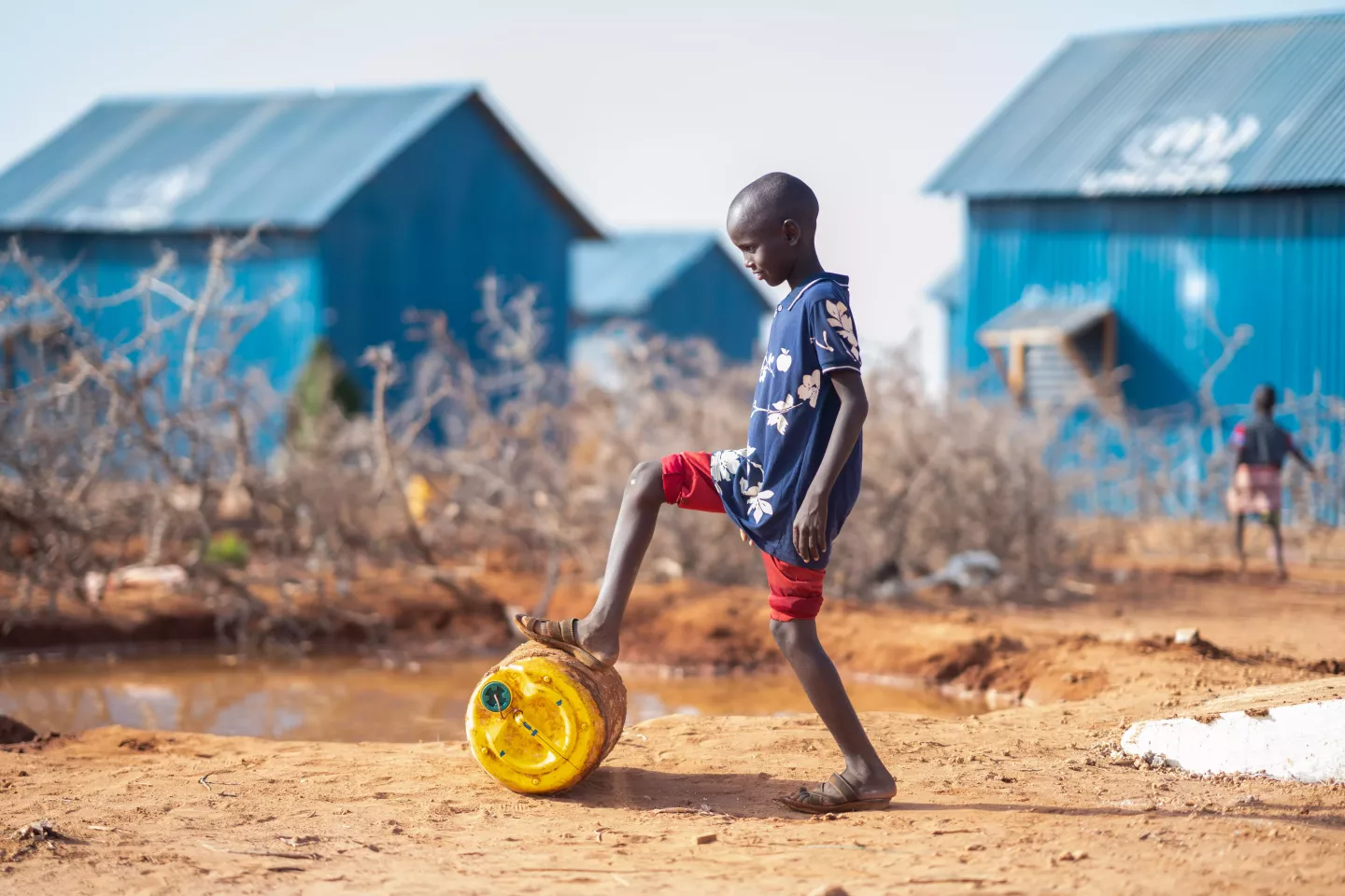 A boy rolls a jug along the ground. Somalia