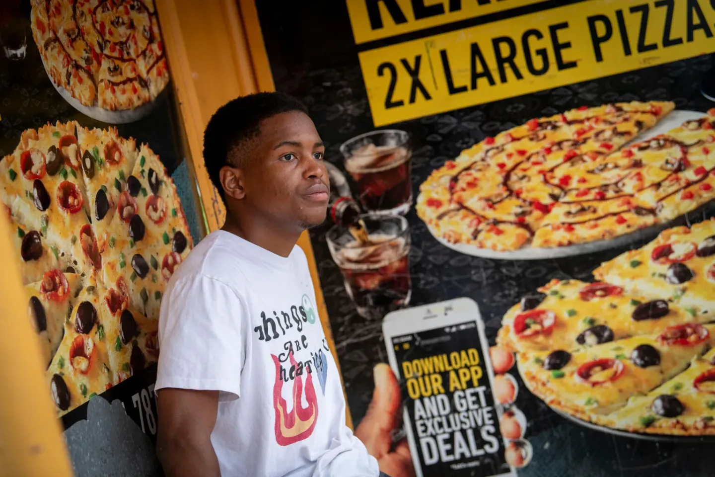 Lulutho (Lulu) Madolo, 19, a student at the &nbsp;University of Pretoria, sits at a bus stop in his hometown of Randburg, Johannesburg, in front of large signs advertising pizza.