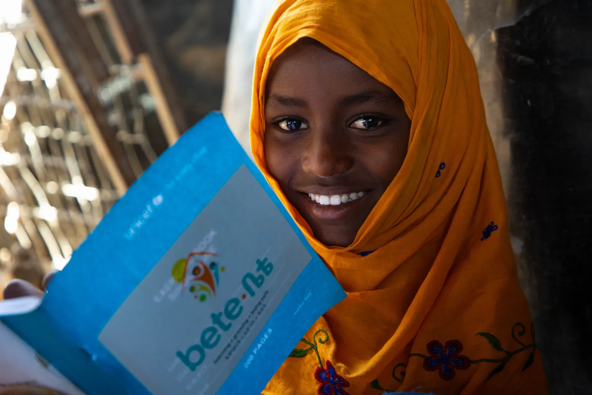 Smiling Mariam, poses for a photo, looking directly at the camera, while holding a book in her hand