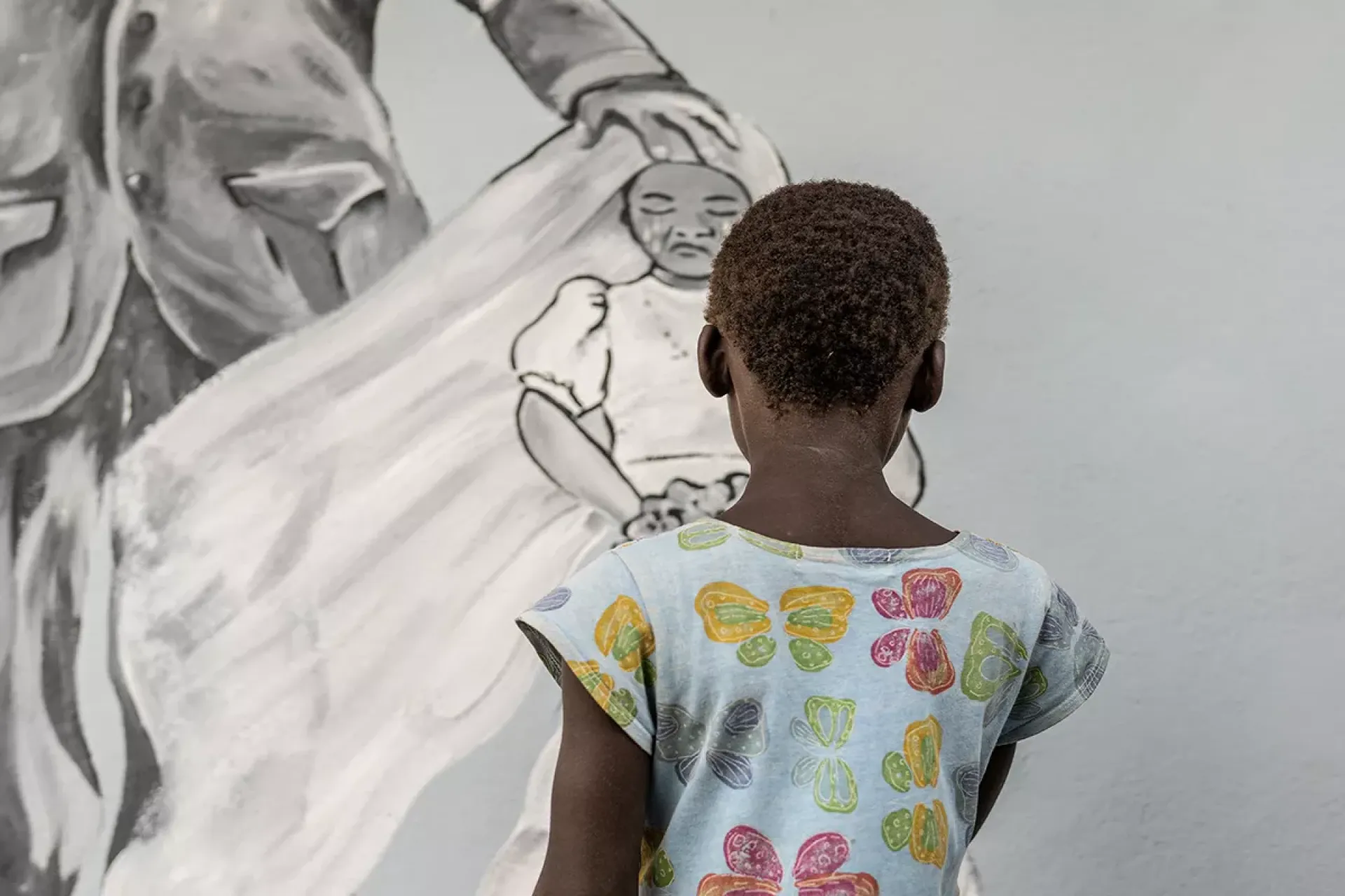A little girls look on a wall mural illustrating two scenarios lived by the children in rural communities. One scenario illustrates what are the rights of children and the other illustrates a more complex issue, child marriage. 