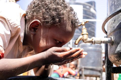 A child drinks water from hands cupped under a tap