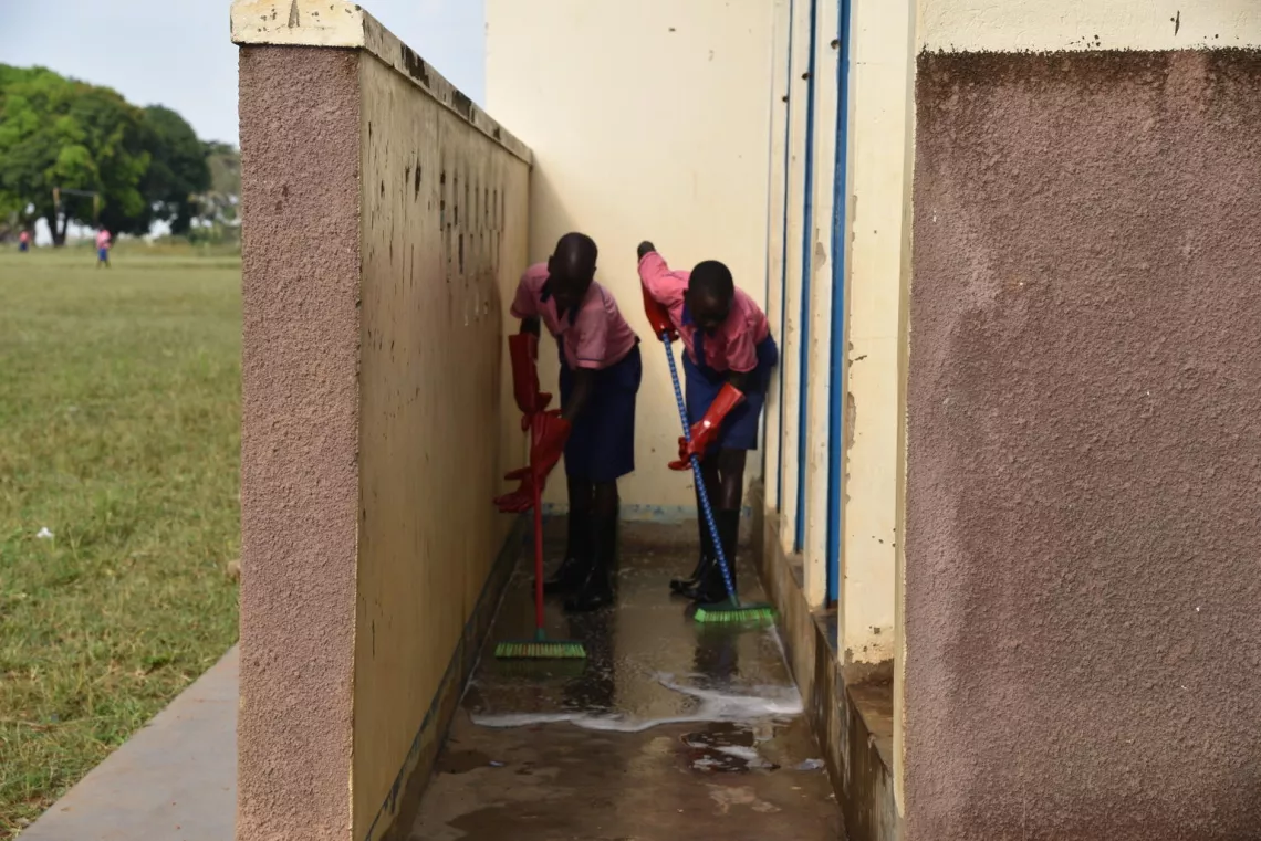 Two students in Uganda mop the floor outside a lavatory