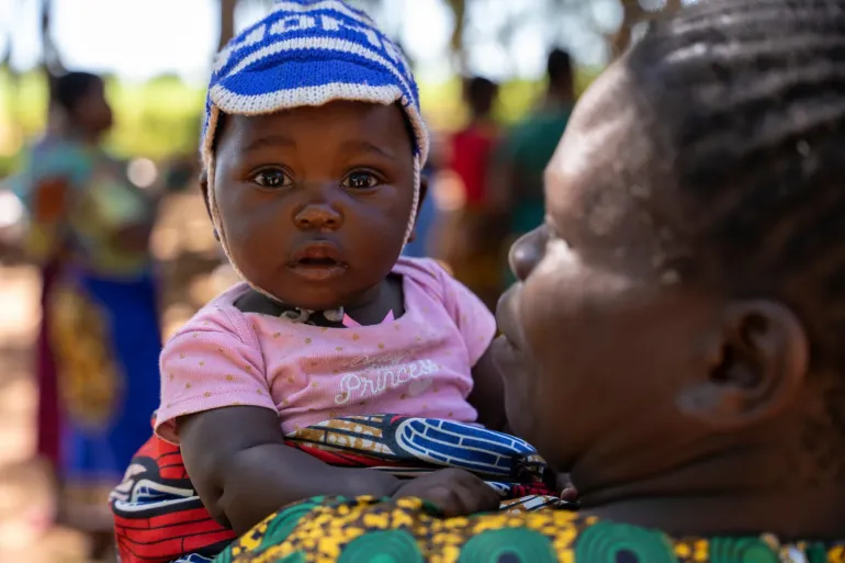 On 30 January 2024, a child is held by her parent at the vaccination site during Rebecca's outreach visit to Chinkuyu village.