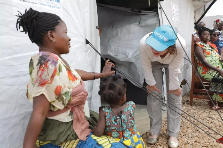 A mother sits with her child in her lap while speaking to a UNICEF staff