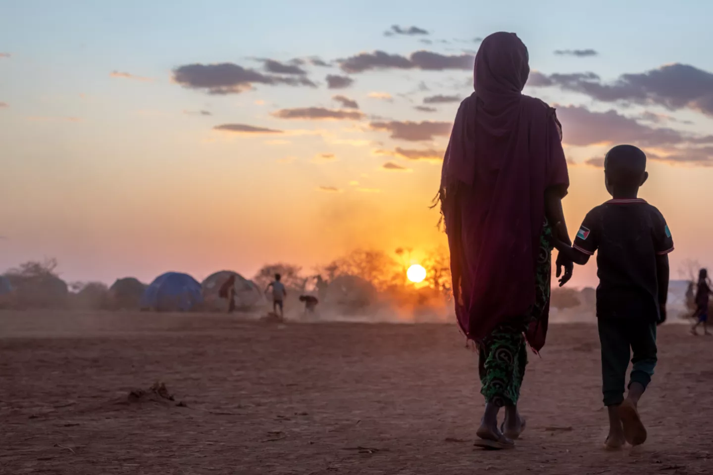 A mother and a child walk together in Bul'ad IDP camp as the sun sets in the horizon. 