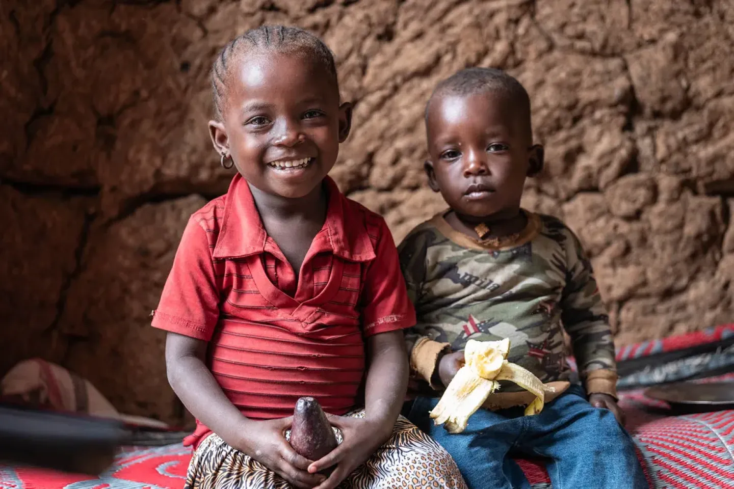 A little girl and a little boy sitting next two each other and looking straight at the camera