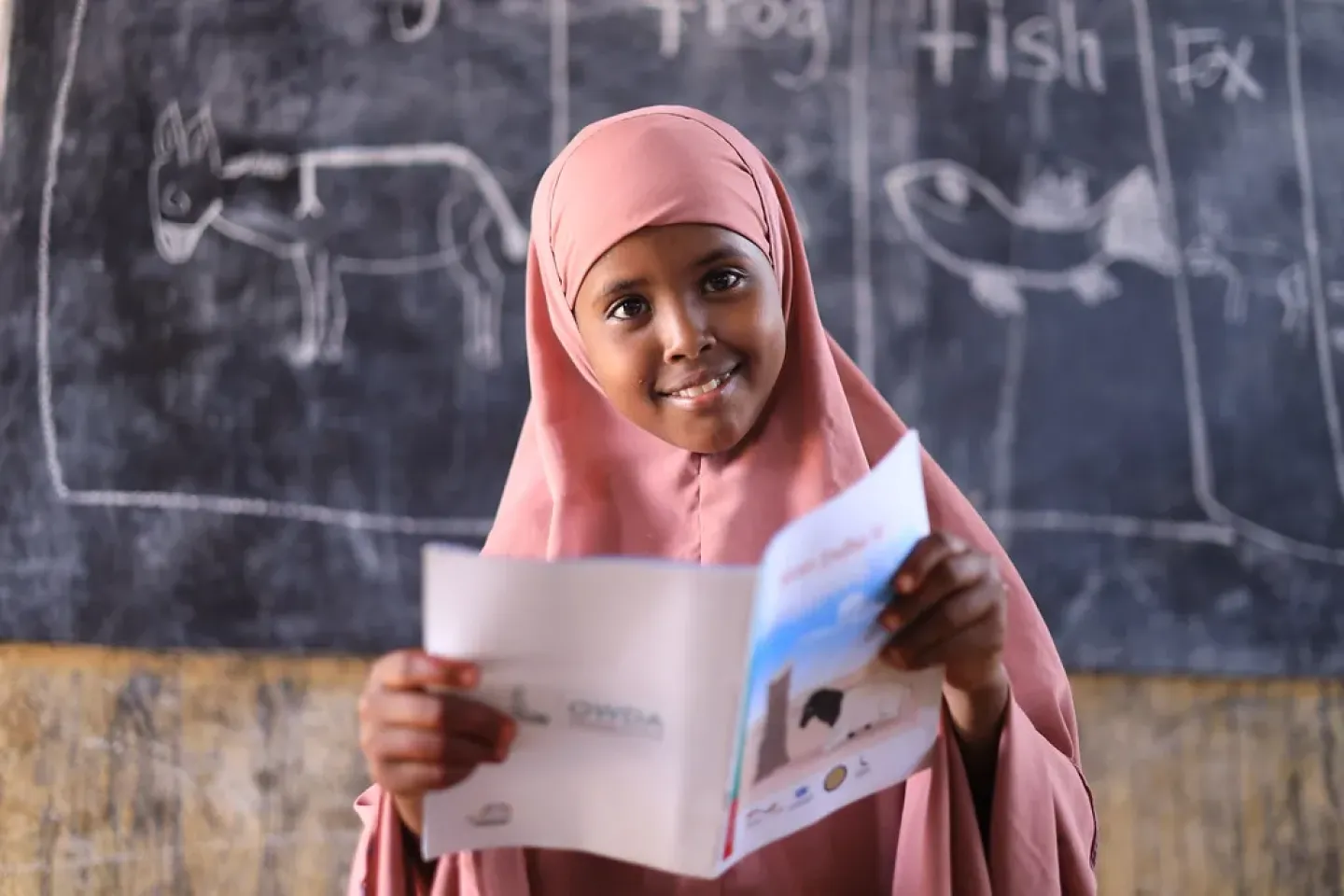 A young girl holding her notebook in front of her  classroom 
