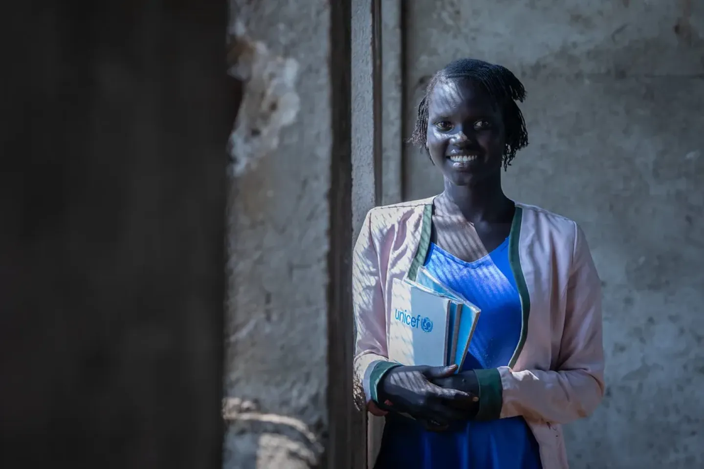A young girl standing in fornt of a window with her text book in her hand