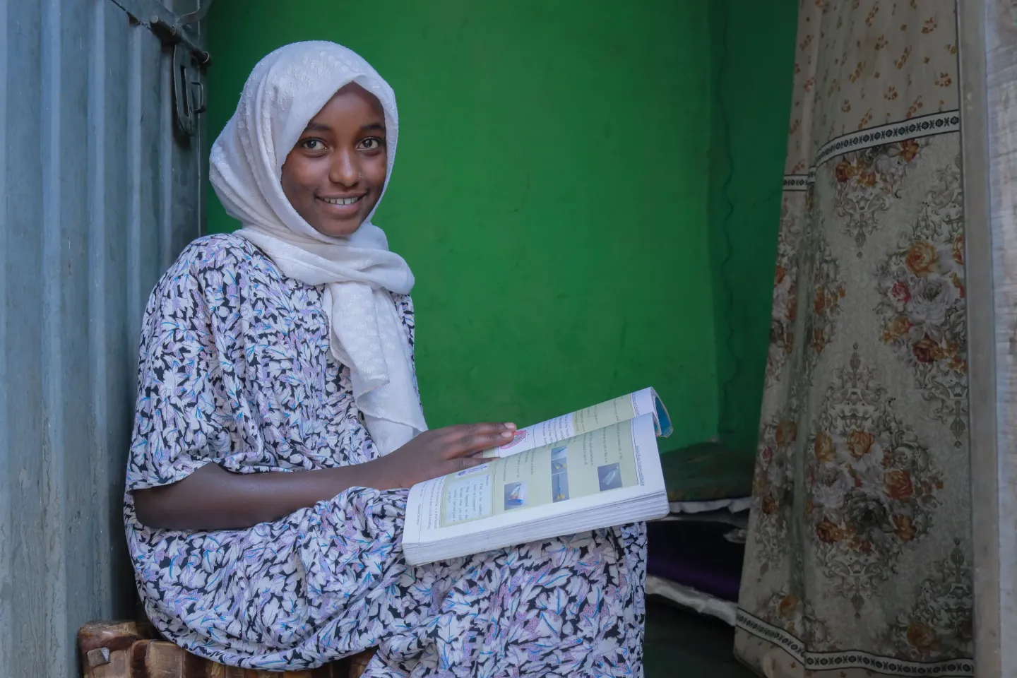 A young girl reads her book inside her house and siting by the door