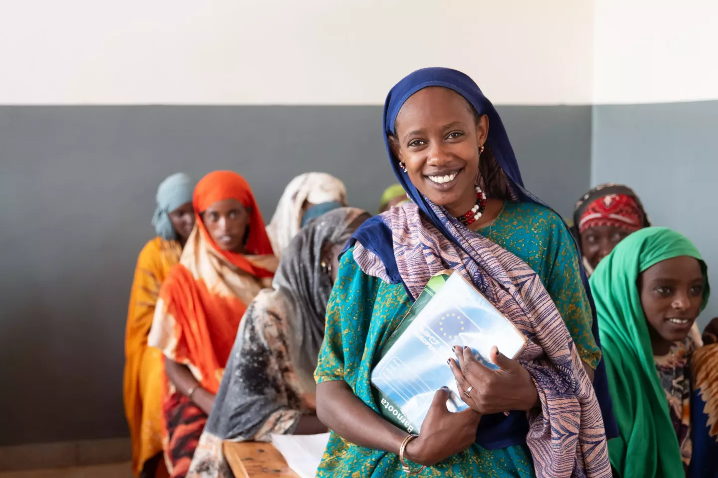 A girl in a classroom holding her book.