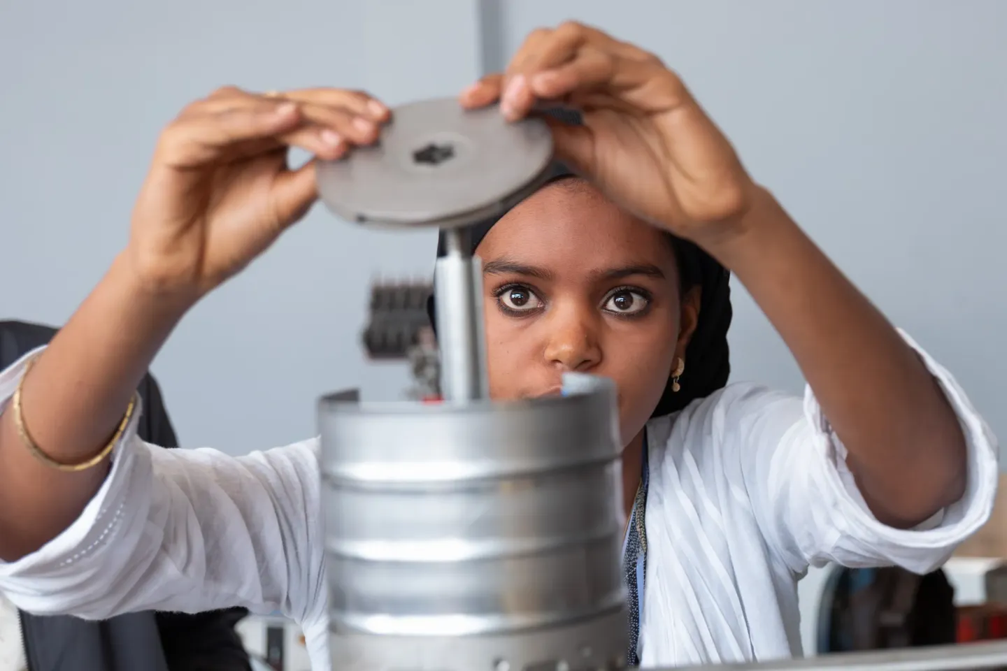 A young woman assembles a water pump inside a maintenance room.  