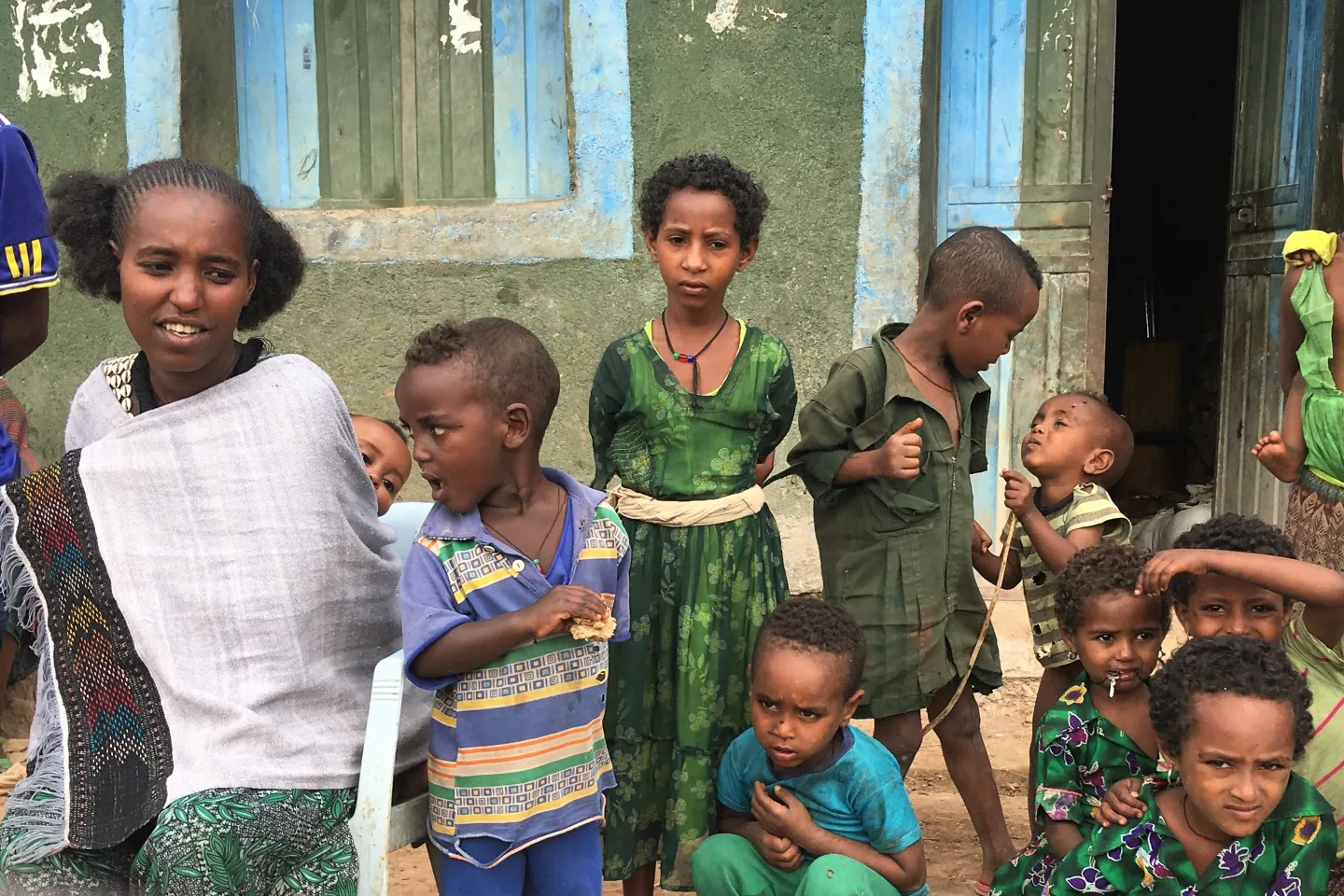 Nigist on the left with her youngest child on the back describing how she takes care of her two children whilst other children from the community come close curiously. 