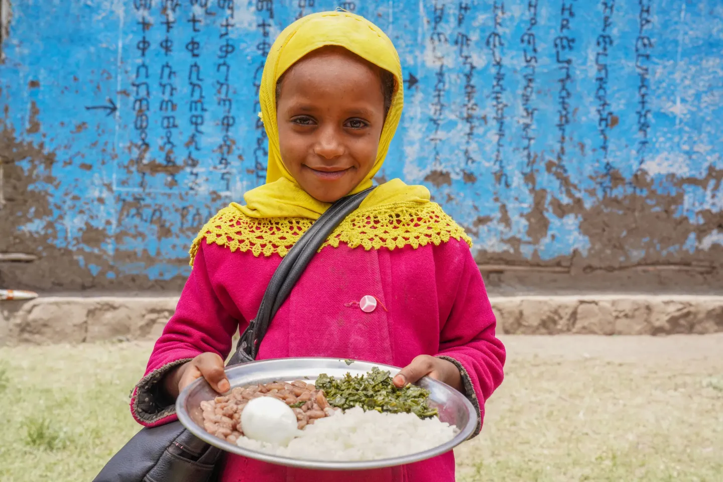 A six year old girl smiles while holding a plate full of rice and boiled egg. 