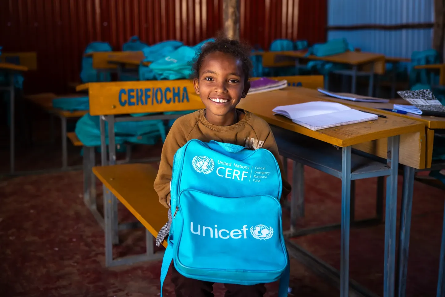 Adiam holding sitting in her classroom holding her backpack.