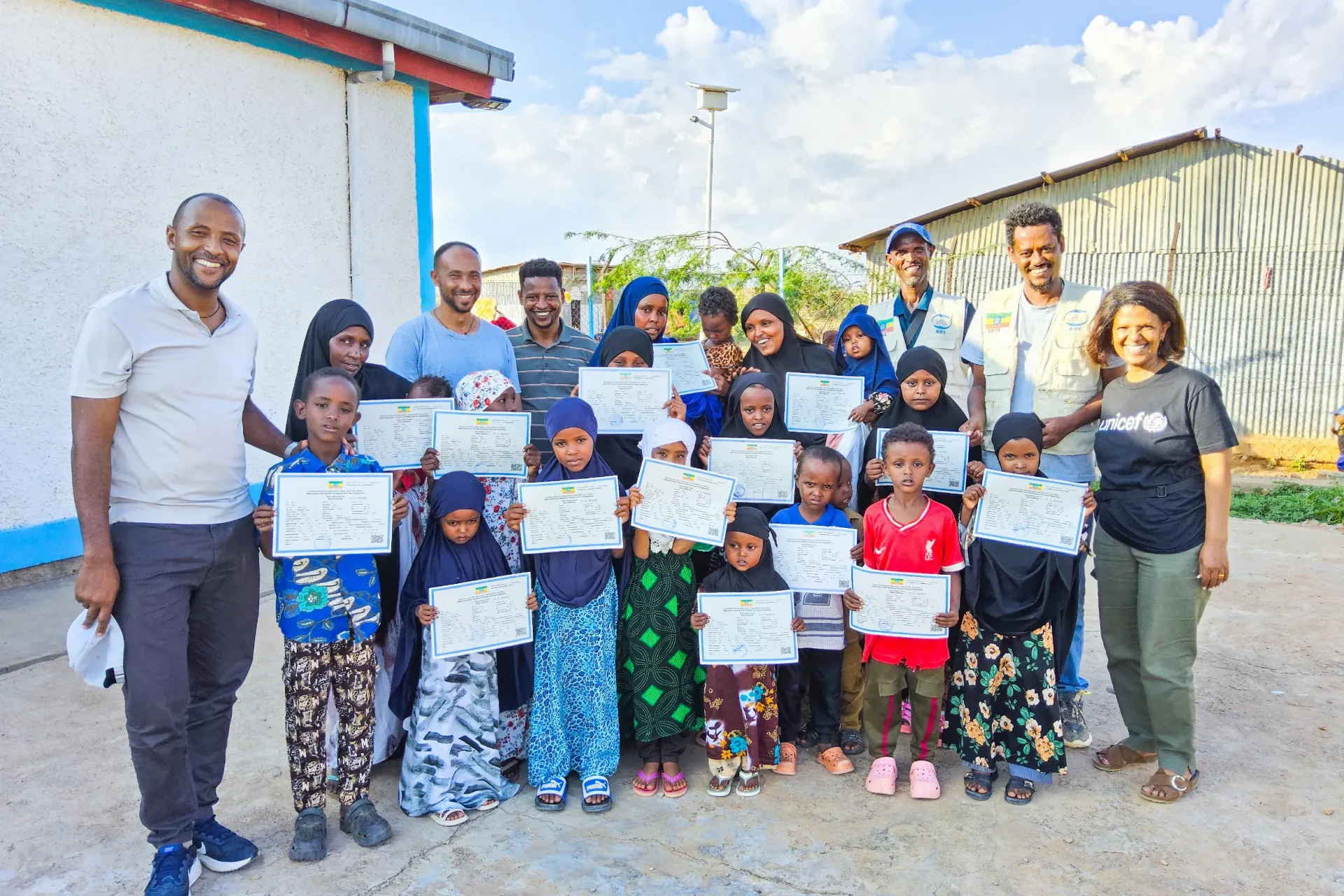 A group of children and mothers standing together for a group photo holding birth certificates
