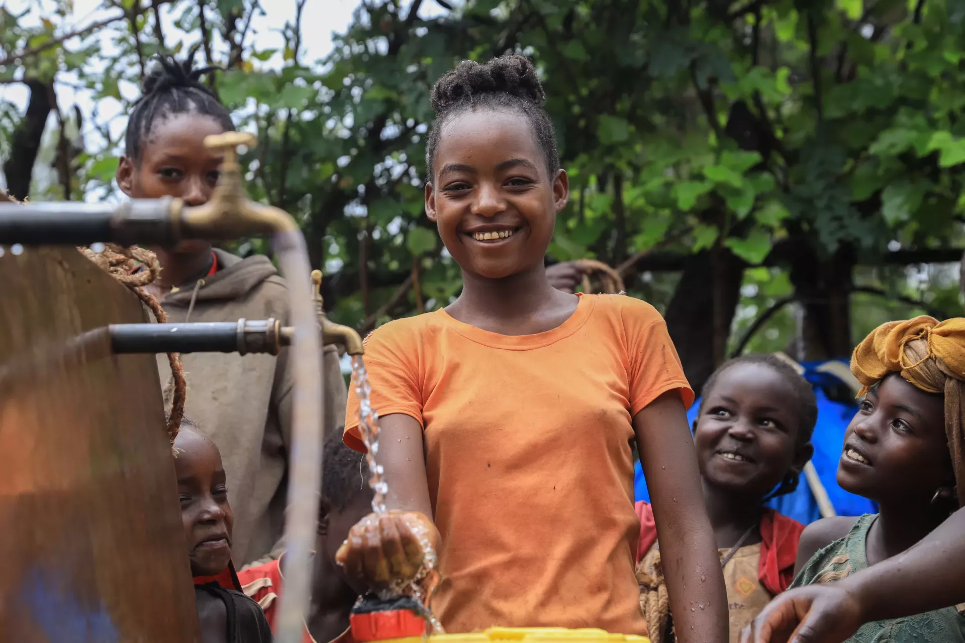 A girl stands next to a water tap smiling.