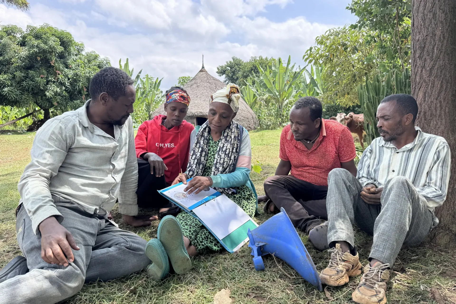 A women sitting on the ground with three men and one women, and explaining about the products her enterprises is producing