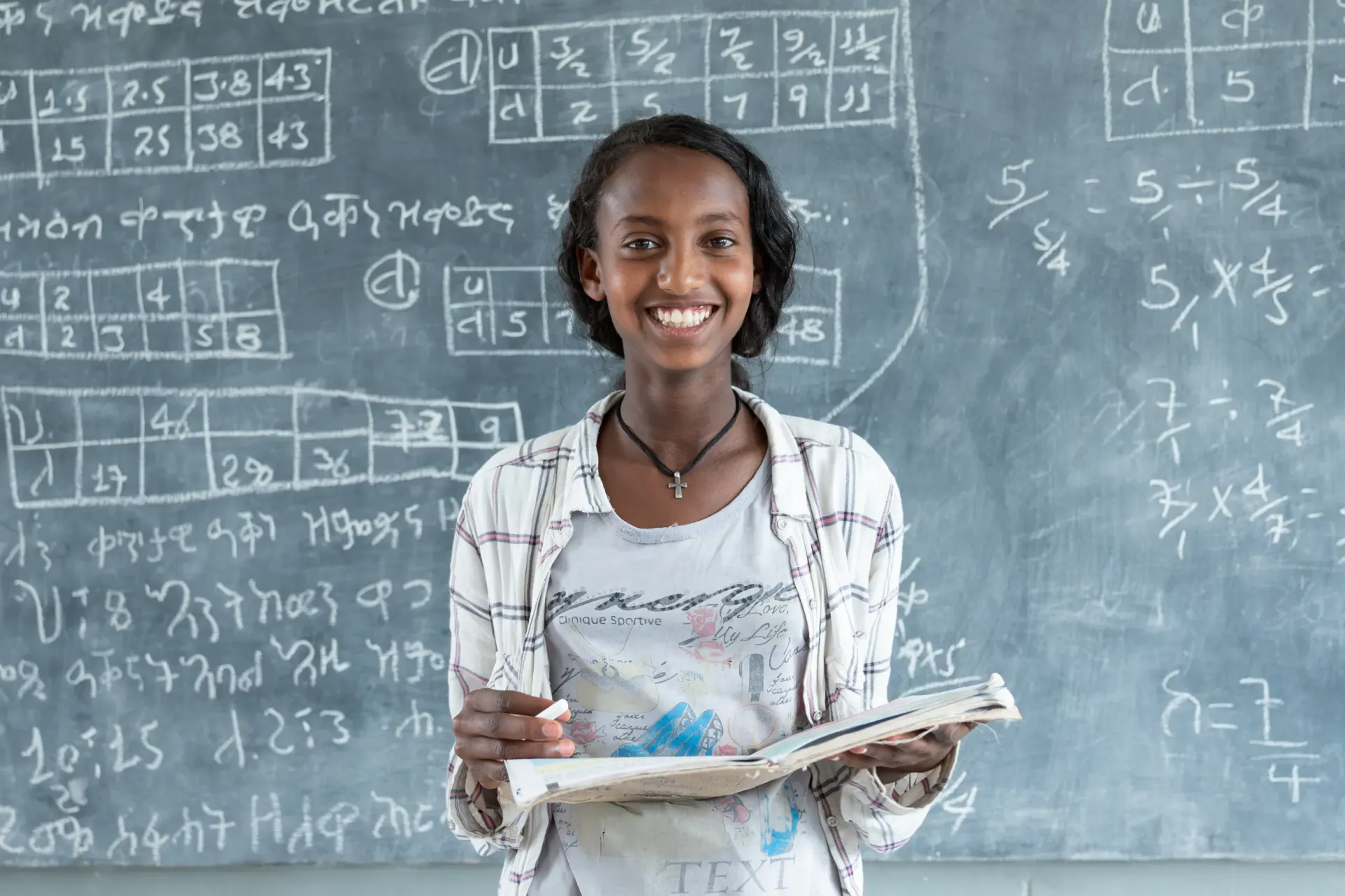 A young girls smiles holding her book in font of class