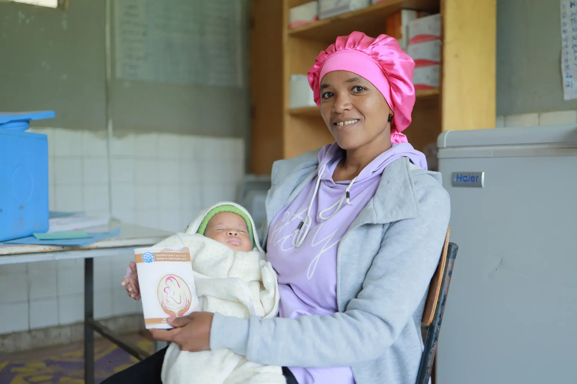 A mother holding her baby in her hand and showing her baby's vaccine card